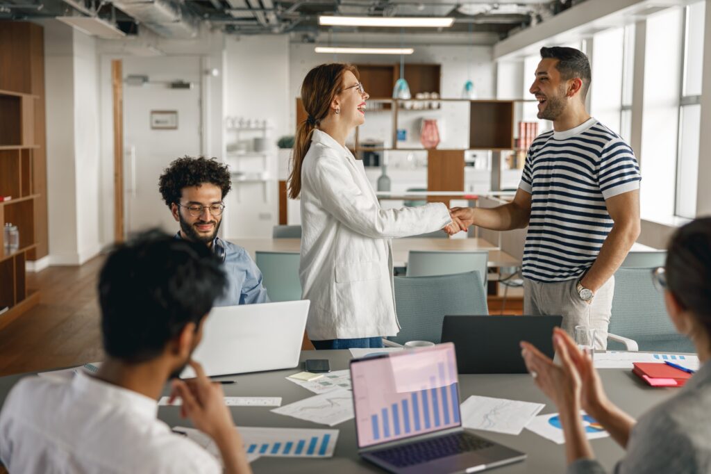 Smiling female boss leader shaking hand of new team member recruiting him for job on staff briefin